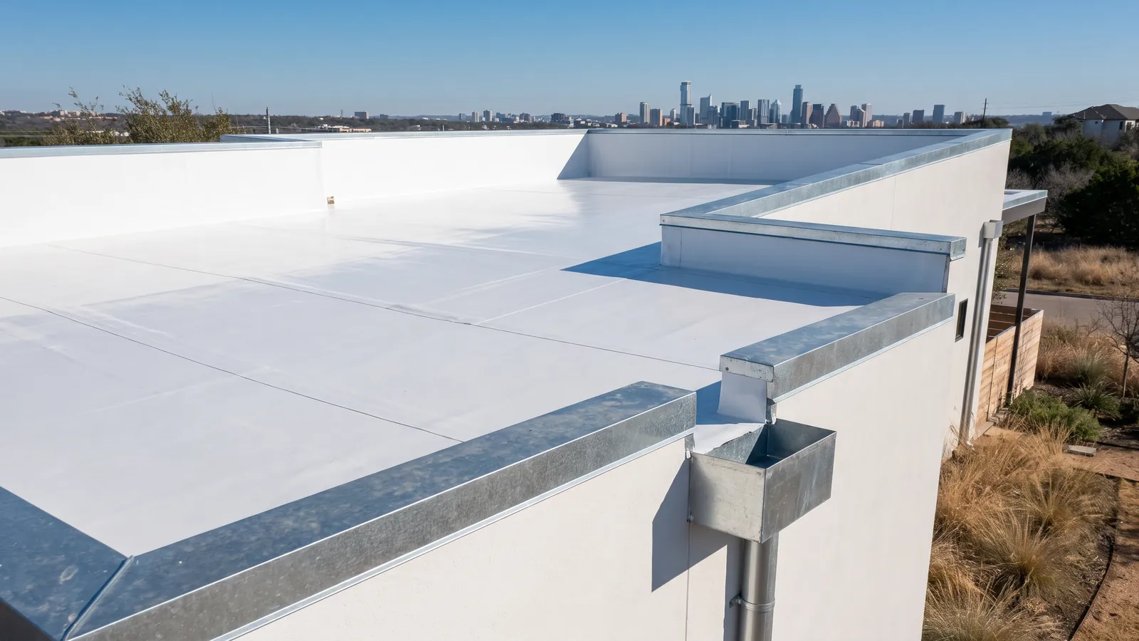 White single-ply membrane on the flat roof of a modern East Austin home, parapet walls and a scupper, downtown towers faint in the distance